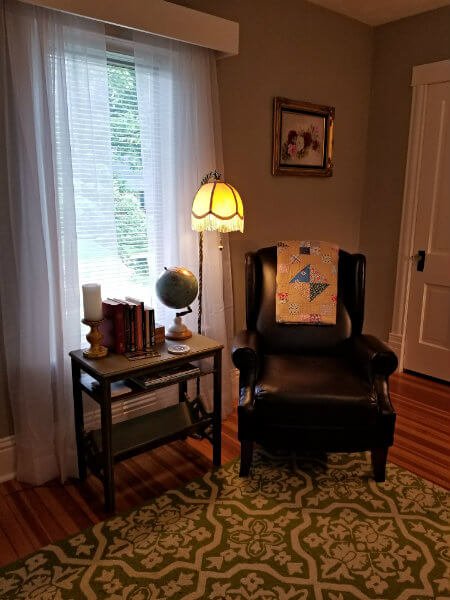 Gray room with wood floor, area rug, dark leather chair, table lamp and side table with books and a globe