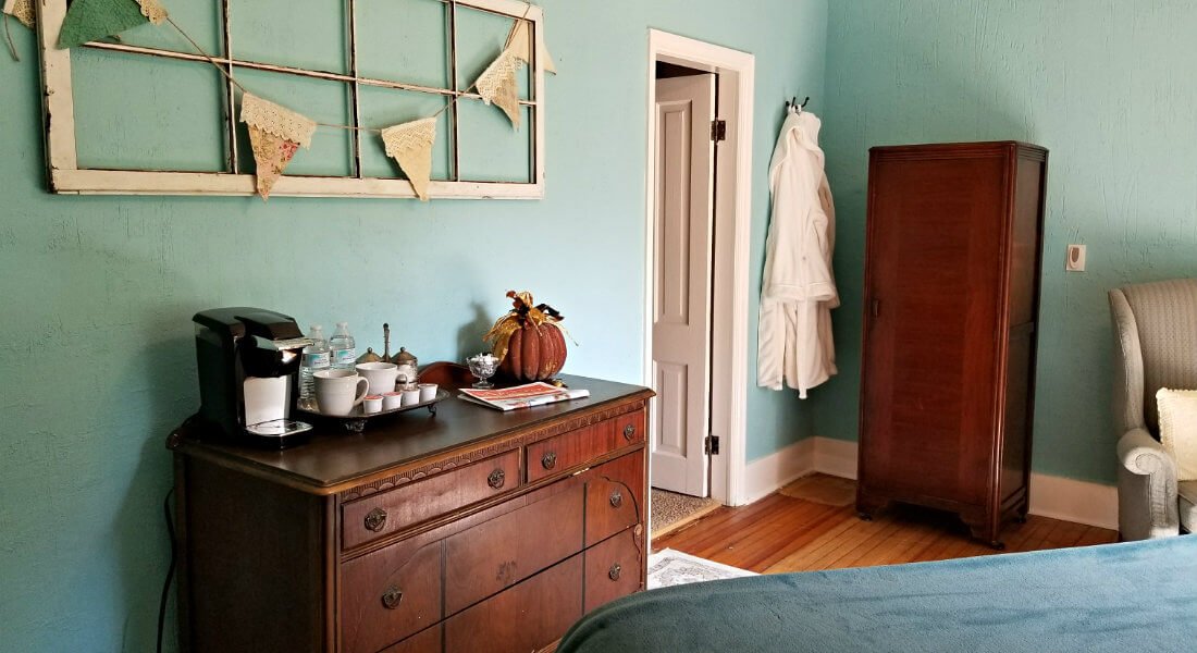 Blue room with white trim, wood floors, wood dresser and hanging white robe