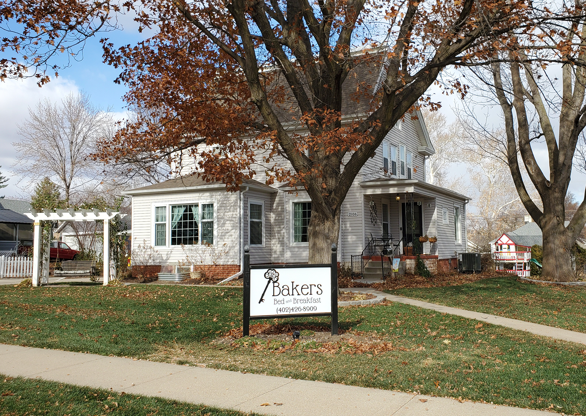Exterior view of the B&B with tan siding, lots of windows, surrounded by green grass, shrubs and flowers
