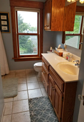 Blue painted bathroom with tile floor, stained wood, wood vanity with mirror and a window